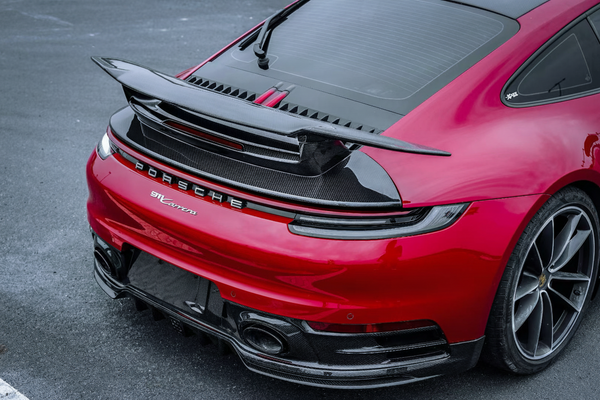 A striking rear view of a red 992.1 Porsche 911, featuring an extended performance wing and a sculpted rear diffuser. A clean, purposeful silhouette that blends motorsport precision with modern Porsche design.